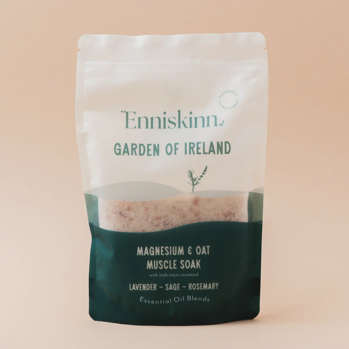 A stand-up pouch of Enniskinn Garden of Ireland Magnesium & Oat Muscle Soak, featuring a white upper section and a dark teal lower section, set against a solid pale peach background.