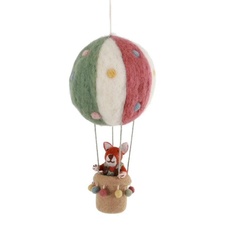 A handcrafted felted wool hot air balloon ornament featuring a green, white, and red striped balloon with colorful felted dots, and a small fox figurine sitting in a tan basket below, suspended against a plain white background.