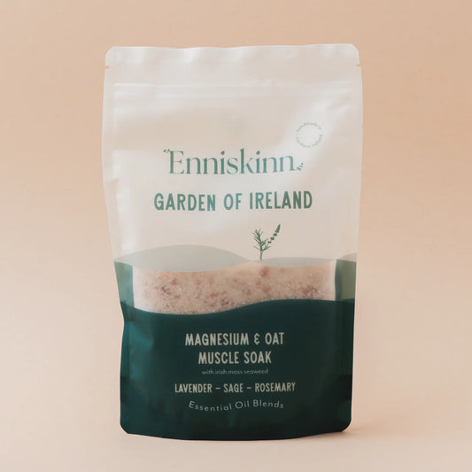 A stand-up pouch of Enniskinn Garden of Ireland Magnesium & Oat Muscle Soak, featuring a white upper section and a dark teal lower section, set against a solid pale peach background.