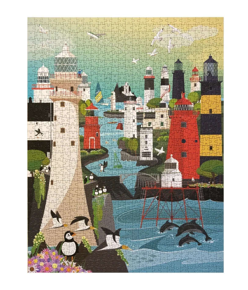 A completed jigsaw puzzle featuring a whimsical coastal lighthouse scene with penguins, dolphins, birds, and colorful buildings along the shoreline. Blue moon gifts Duncannon wexford