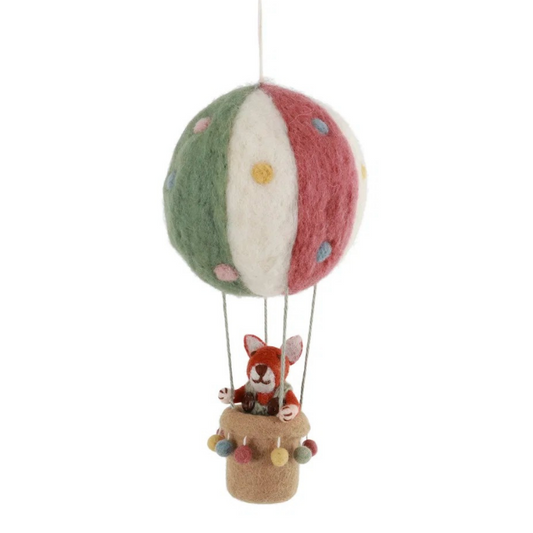 A handcrafted felted wool hot air balloon ornament featuring a green, white, and red striped balloon with colorful felted dots, and a small fox figurine sitting in a tan basket below, suspended against a plain white background.