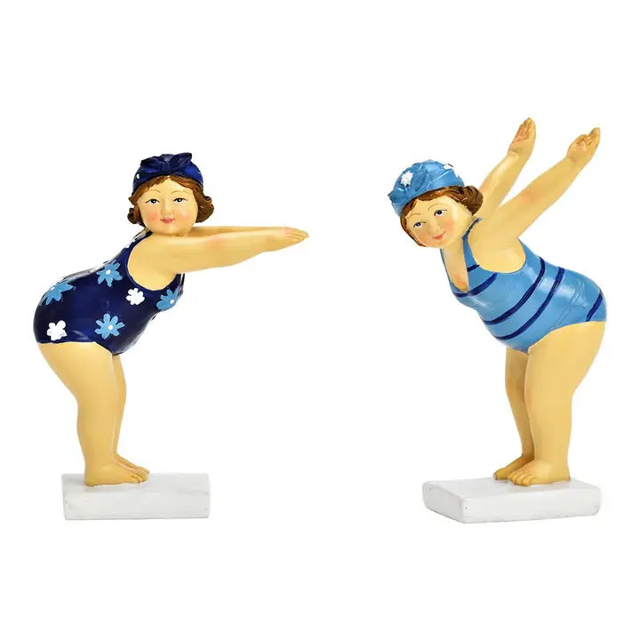 Two decorative figurines of a mother and daughter swimming together, one in a navy blue swimsuit with white flowers and the other in a blue and navy striped swimsuit, both standing on white bases against a white background.