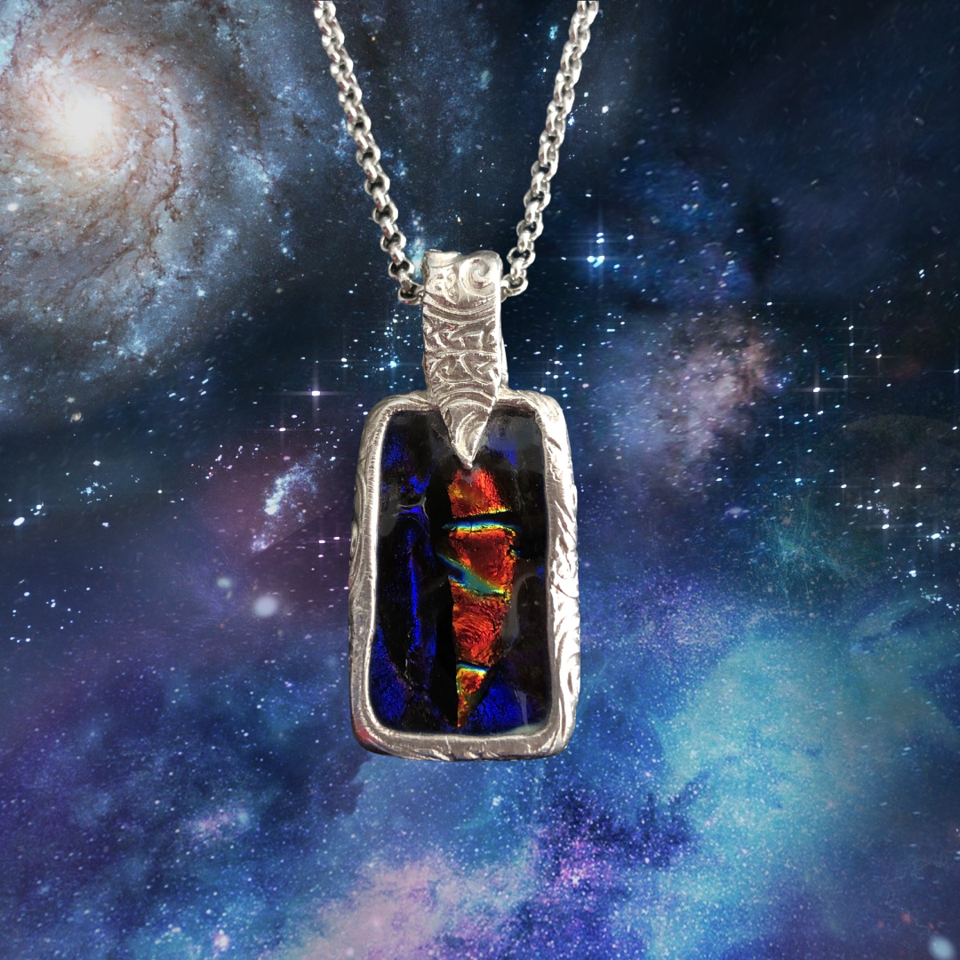 A silver metal clay glass pendant with a Celtic design, featuring a layered multicolored glass pattern, displayed against a celestial background with stars and a nebula.